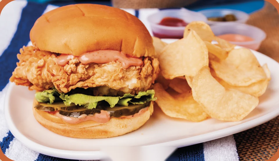 Crave Chicken Burger: hamburguesa de pechuga de pollo empanizada con lechuga y pepinillos, con papas fritas